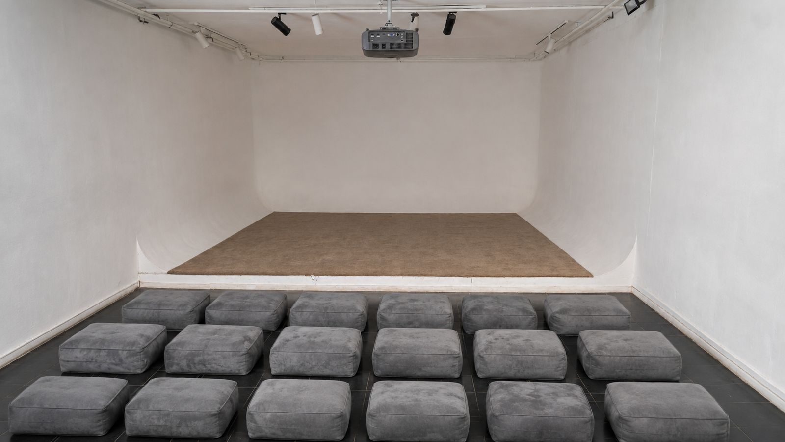 Sinema Siri cinema room — cushion seating, ceiling projector, white cyclorama walls and low stage